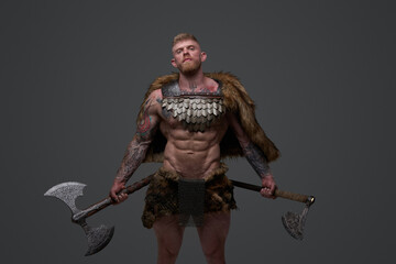 Fototapeta na wymiar Proud viking dressed in fur and armor holding two axes