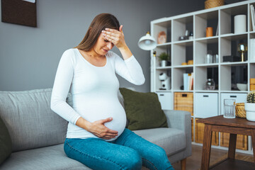 Fototapeta na wymiar A frustrated young woman who suffers from a headache while at home with the expression that she is not well, with her eyes closed. The concept of pregnancy and pain