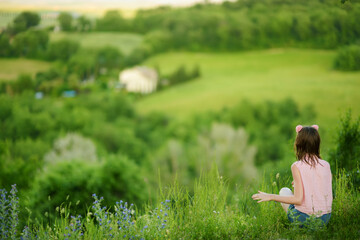 Young girl admiring the view of green fields and farmlands with small villages on the horizon. Summer rural landscape surrounding Pienza town, Tuscany, Italy.