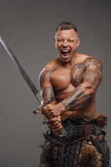 Fototapeta na wymiar Violent warrior with tattoos holding sword against gray background