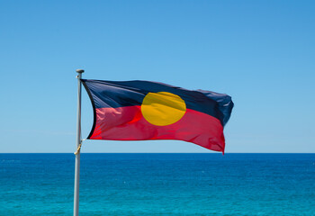 Australian aboriginal flag waving with blue sky and ocean water at the background.