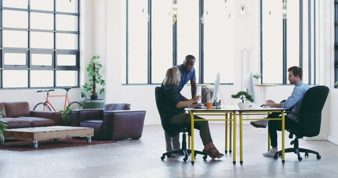 They work seamlessly together. African american business man talking to mature business woman at her desk, discussing work and looking at computer. Diverse group of three in modern office