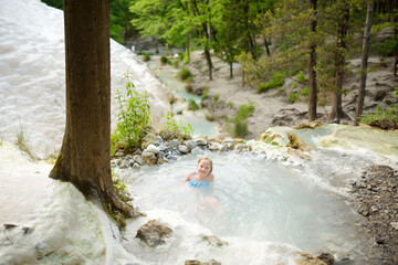 Young girl bathing in Bagni San Filippo, small hot spring containing calcium carbonate deposits, forming white concretions and waterfalls. Geothermal pools and hot springs in Tuscany, Italy. - obrazy, fototapety, plakaty