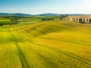Stunning aerial view of yellow fields and farmlands with small villages on the horizon. Rural landscape of rolling hills, curved roads and cypresses of Tuscany, Italy.