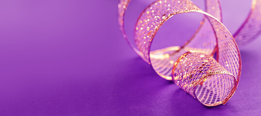 A swirl of golden gift ribbon on lilac violet for St Valentines day birthday gift or Christmas. Minimal with copy space. Mothers Day or wedding