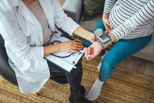 Doctor measuring blood pressure of young pregnant woman, close up. Eclampsia of pregnant women concept. Young doctor is checking blood pressure of pregnant woman at home. 