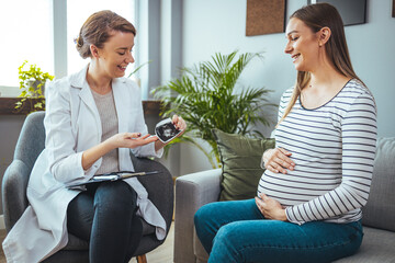 Fototapeta premium The doctor shows a sonographic picture of the baby while sitting on the sofa at home, shows the first photo of her child, enjoys a happy maternity leave.