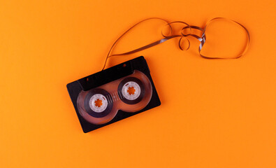 Audio cassette with pulled out audiotape on orange background