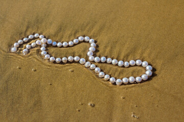 Pearl beads lie on the sand in the water of the bay