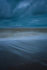 The sea wave is a blurry movement. A storm on a sandy beach. Huge waves at long exposure. Atmospheric natural background. The concept of bad weather, heavy rains, hurricane wind. Abstract Ocean