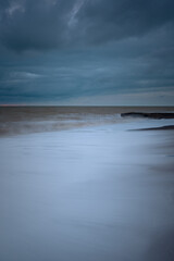 The sea wave is a blurry movement. A storm on a sandy beach. Huge waves at long exposure. Atmospheric natural background. The concept of bad weather, heavy rains, hurricane wind. Abstract Ocean