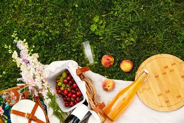 leisure and drinks concept - close up of food, drinks and basket on picnic blanket on grass