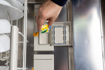 A hand puts a dishwasher tablet in a special cell. The woman turns on the built-in dishwasher.