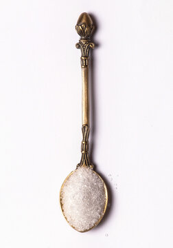 A spoonful of sugar in an antique spoon on white background.