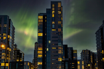 Aurora Borealis over the capital of Iceland. Modern high-rise buildings in central Reykjavik at night with the Northern Lights in the background. - obrazy, fototapety, plakaty