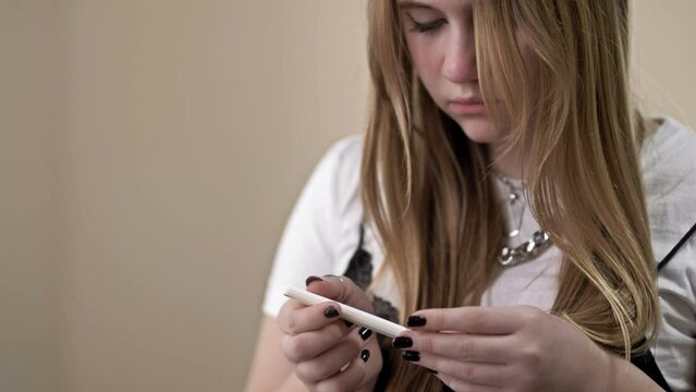 Teenage girl looks fearfully at a pregnancy test.