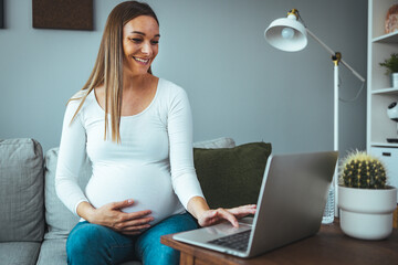 Pregnant businesswoman with hand on stomach working at desk. Female professional is wearing...