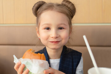 child in fast food restaurant. little girl with appetite eating hamburger. Kids eat unhealthy fast...