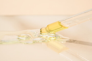 Pipette with serum or liquid yellow gel on light beige glass background. Beauty cosmetic concept