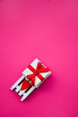 A gift for a happy Valentine's day. A gift box with a red ribbon on a white sled with a red heart on a pink background. A greeting card. The concept of February 14. Love