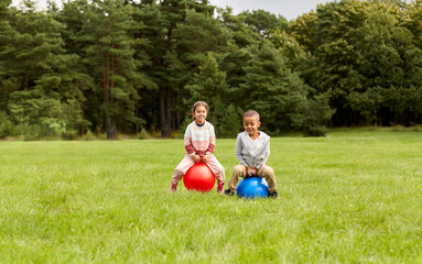 childhood, leisure and people concept - happy children bouncing on hoppers or bouncy balls at park