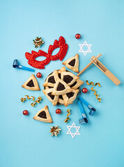 Purim homemade hamantaschen cookies, red carnival mask, noisemaker, sweet candies and party decor on blue background.