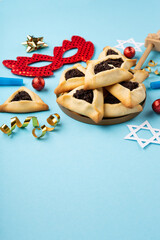 Obraz na płótnie Canvas Purim homemade hamantaschen poppy seed cookies, red carnival mask, noisemaker, sweet candies and party decor on blue background.