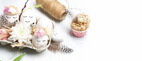 Fototapeta na wymiar Easter holiday concept with cute handmade white eggs, tree branches, quail feathers and spring flowers on white wooden background.