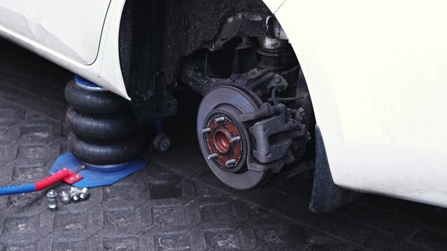 Car Wheel Hub with Brake Disc and Brake Pad Exposed during Tyre Change at Garage Workshop with Lug Nuts and Wrench Laying on Ground