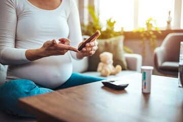 Obraz na płótnie Canvas Happy Pregnant woman with glucometer checking blood sugar level at home. Woman testing for high blood sugar. Pregnant Woman holding device for measuring blood sugar...