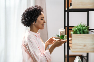 home improvement and decoration and people concept - happy smiling young woman placing candles to shelf