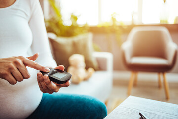 Pregnancy, health and glycemia concept - pregnant beautiful woman checking blood sugar level with...