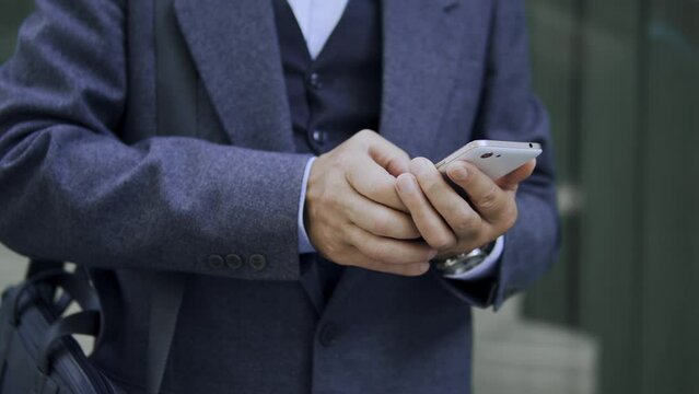 Businessman in elegant coat typing on smartphone, checking his bank account