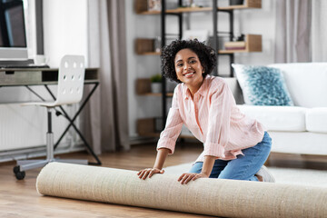 household, home improvement and interior concept - happy smiling young woman unfolding carpet on floor