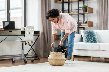 household, home improvement and cleaning concept - happy smiling young woman with blanket and wicker basket sitting on floor