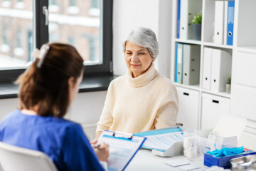 Obraz premium medicine, health and vaccination concept - doctor with clipboard and senior woman at hospital