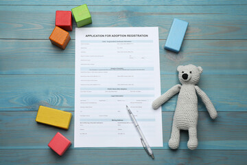 Adoption application, toy bear, colorful cubes and pen on blue wooden table, flat lay