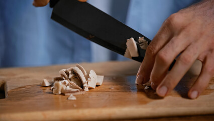 cropped view of man cutting mushrooms on chopping board in kitchen.