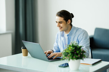 Happy young man works on his laptop to get all his business done early in the morning