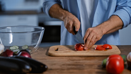 cropped view of man cutting ripe tomatoes near blurred eggplants.