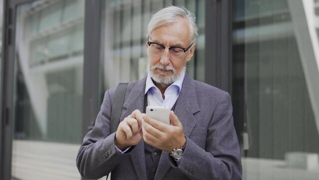 Gray-bearded businessman looking through contract on smartphone before meeting
