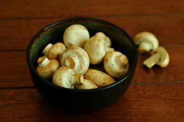 A bowl full of white button mushrooms on wooden background.