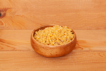  Uncooked pasta in wooden bowl on wooden background.