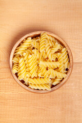  Uncooked pasta in wooden bowl on wooden background.