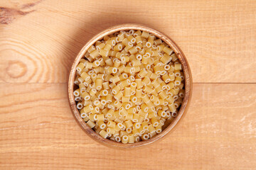  Uncooked pasta in wooden bowl on wooden background.