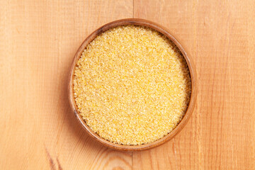Raw broken organic wheat grains on wooden background and in wooden bowl.
