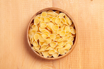  Uncooked pasta in wooden bowl on wooden background.