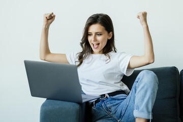 Happy young woman laughs with joy, raising hands and looking at laptop. Overjoyed female student celebrating achievement. Online bid win, winner, discount coupon or online home shopping concept.