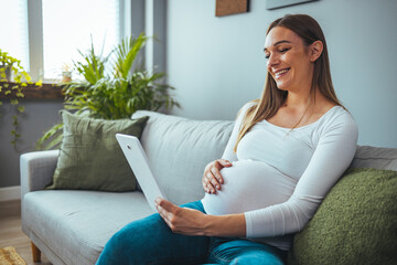 Obraz premium Smiling pregnant young woman lying on bed and using tablet at home. Pregnancy, technology, people and expectation concept - close up of pregnant woman with tablet pc computer in bed at home