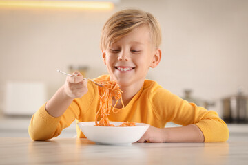 Happy boy eating tasty pasta at table in kitchen